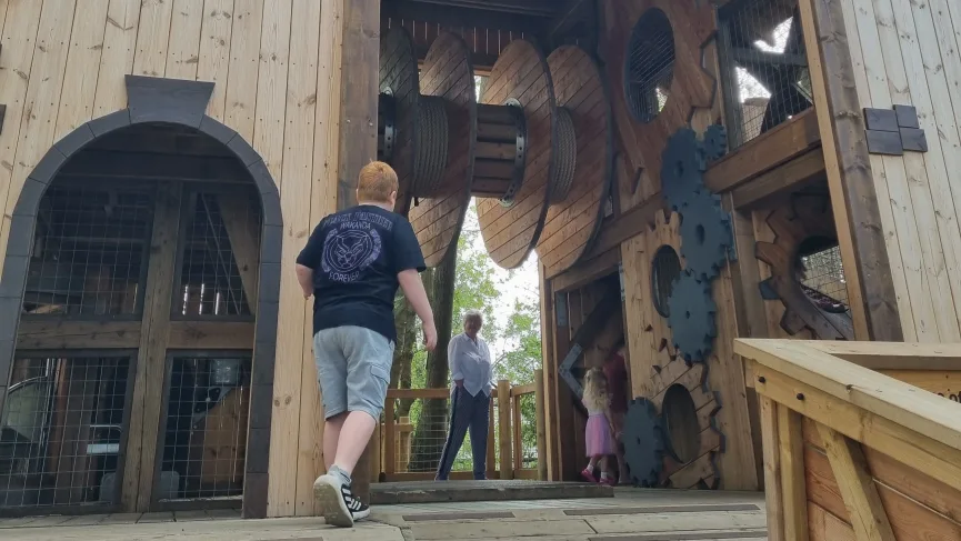Child approaching a wooden play structure with large gears, representing curiosity, growth, and small moments of peace in a busy family life.